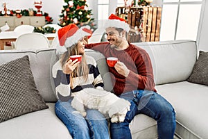Young hispanic couple wearing christmas hat drinking coffee