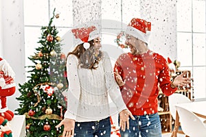 Young hispanic couple wearing christmas hat throwing conffeti celebrating new year at home