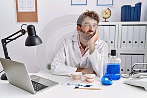 Young hispanic dentist man working at medical clinic thinking looking tired and bored with depression problems with crossed arms