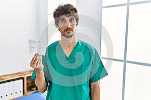 Young hispanic doctor man holding covid record card looking sleepy and tired, exhausted for fatigue and hangover, lazy eyes in the