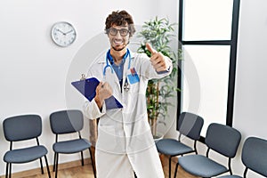 Young hispanic doctor man at waiting room approving doing positive gesture with hand, thumbs up smiling and happy for success