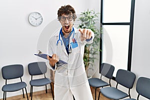 Young hispanic doctor man at waiting room pointing displeased and frustrated to the camera, angry and furious with you