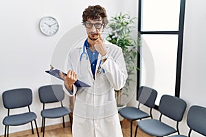 Young hispanic doctor man at waiting room pointing to the eye watching you gesture, suspicious expression