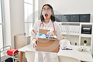 Young hispanic doctor woman holding box with medical items angry and mad screaming frustrated and furious, shouting with anger
