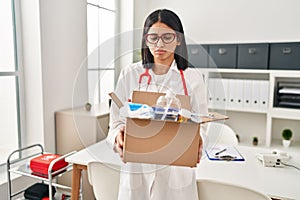 Young hispanic doctor woman holding box with medical items depressed and worry for distress, crying angry and afraid