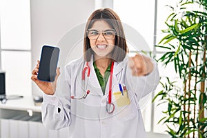 Young hispanic doctor woman showing smartphone screen annoyed and frustrated shouting with anger, yelling crazy with anger and