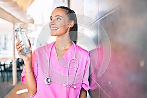 Young hispanic doctor woman using hand sanitizer gel leaning on the wall at street of city