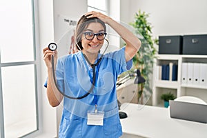 Young hispanic doctor woman wearing stethoscope at the clinic stressed and frustrated with hand on head, surprised and angry face