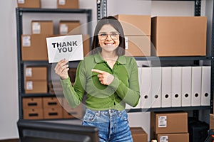 Young hispanic doctor woman working at small business ecommerce holding thank you banner smiling happy pointing with hand and