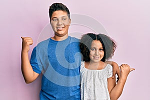 Young hispanic family of brother and sister wearing casual clothes together pointing to the back behind with hand and thumbs up,