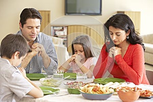 Young Hispanic Family Saying Prayers Before Meal At Home