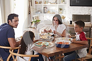 Young Hispanic family sitting at dining table eating dinner together