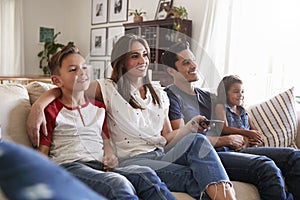 Young Hispanic family sitting on the sofa at home watching TV togther, close up photo