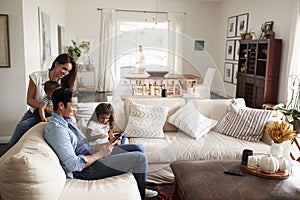 Young Hispanic family sitting on sofa reading a book together in their living room