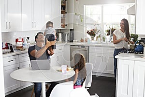 Young Hispanic family in their kitchen, dad holding baby in the air, mum cooking at the hob