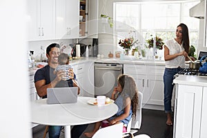 Young Hispanic family in their kitchen, dad holding baby, mum cooking at the hob