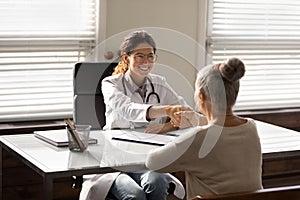 Young hispanic female doctor shake hand of elderly woman patient