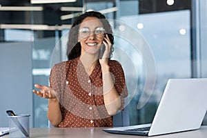 Young hispanic female freelancer wearing glasses sitting in office at desk with white laptop