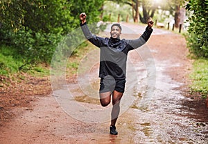 Young hispanic fit male athlete cheering with his fists in the air while on a run in a forest in the rain outside in