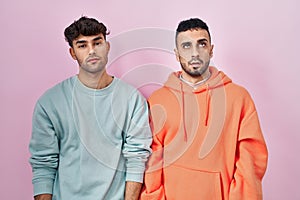 Young hispanic gay couple standing over pink background looking sleepy and tired, exhausted for fatigue and hangover, lazy eyes in
