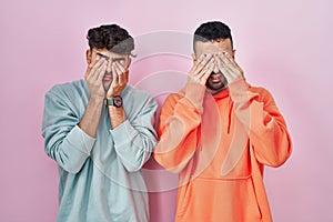 Young hispanic gay couple standing over pink background rubbing eyes for fatigue and headache, sleepy and tired expression