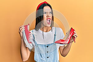 Young hispanic girl choosing high heel shoes and sneakers angry and mad screaming frustrated and furious, shouting with anger