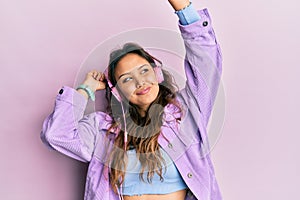 Young hispanic girl dancing and listening to music using headphones smiling looking to the side and staring away thinking