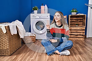 Young hispanic girl doing laundry smiling with happy face winking at the camera doing victory sign