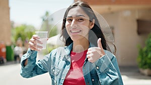 Young hispanic girl drinking water doing ok gesture at street