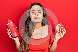 Young hispanic girl eating doughnut and drinking coffee depressed and worry for distress, crying angry and afraid