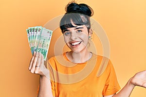 Young hispanic girl holding 50 hong kong dollars banknotes celebrating achievement with happy smile and winner expression with