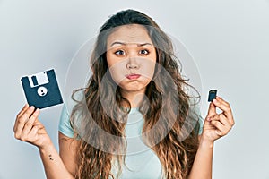 Young hispanic girl holding floppy disk and sdxc card puffing cheeks with funny face