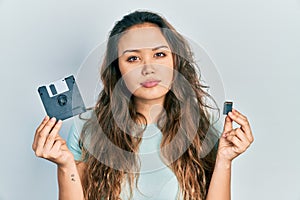 Young hispanic girl holding floppy disk and sdxc card relaxed with serious expression on face
