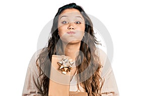 Young hispanic girl holding gifts puffing cheeks with funny face