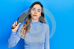 Young hispanic girl holding hairbrush thinking attitude and sober expression looking self confident