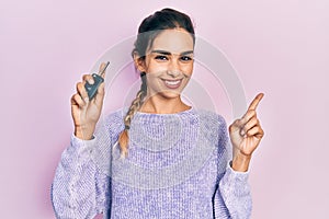 Young hispanic girl holding key of new car smiling happy pointing with hand and finger to the side