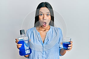 Young hispanic girl holding mouthwash for fresh breath afraid and shocked with surprise and amazed expression, fear and excited