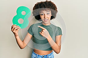 Young hispanic girl holding number eight smiling happy pointing with hand and finger