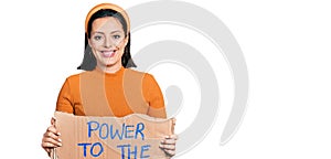 Young hispanic girl holding power to the people banner looking positive and happy standing and smiling with a confident smile