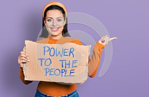 Young hispanic girl holding power to the people banner smiling happy pointing with hand and finger to the side