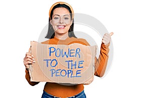 Young hispanic girl holding power to the people banner smiling happy and positive, thumb up doing excellent and approval sign