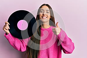 Young hispanic girl holding vinyl disc smiling happy and positive, thumb up doing excellent and approval sign