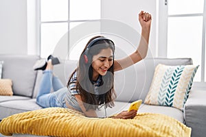 Young hispanic girl listening to music lying on sofa at home