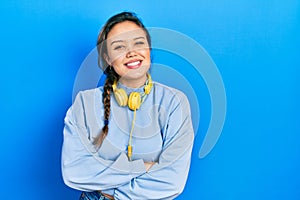 Young hispanic girl listening to music using headphones happy face smiling with crossed arms looking at the camera