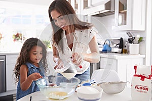 Young Hispanic girl making cake in the kitchen with help from her mum, waist up