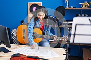 Young hispanic girl musician composing song playing classical guitar at music studio