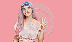 Young hispanic girl with pink hair smiling with happy face winking at the camera doing victory sign