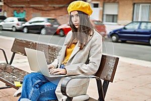Young hispanic girl with serious expression working using laptop at the city