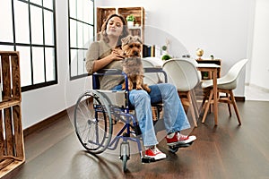 Young hispanic girl sitting on wheelchair at home afraid and terrified with fear expression stop gesture with hands, shouting in