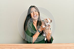 Young hispanic girl smiling happy and hugging dog sitting on the table over isolated white background